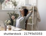 Small photo of Daydreaming. Calm happy young woman floral arranger decorator relaxing at desk with closed eyes. Manager consultant at flower shop leaning back on chair napping enjoying lazy moment with serene smile