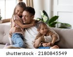 Pleased dad sit on couch with kids, after long separation missed his two little 7s daughters, closing his eyes, hugs them enjoying moment. Family bond and love, Happy Father Day celebration concept