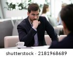 Small photo of Serious young businessman talk with applicant or candidate at job interview feel suspicious doubtful at meeting. Concerned male boss or employer frustrated unsure about client or partner at briefing.