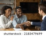 Small photo of Happy African American couple shake hand close deal with male realtor or broker at meeting. Smiling biracial young family man and woman handshake make agreement with real estate agent in office.