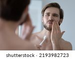 Small photo of Handsome young man look in mirror touch cheek with hand, feels pain while brushing teeth due cavity or caries. Toothache, dental check up, oral care, need toothpaste for sensitive tooth enamel