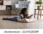 Small photo of Adorable preschooler little Indian girl lying on warm floor using digital tablet in cozy living room, play videogames, watch favourite vlog, spend time at home. Gen Z use modern wireless technology