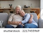 Small photo of Smiling older couple hugging relaxing on sofa look at camera, having pleasant weekend together at home, spend leisure, enjoy rest on couch feel satisfied. Happy marriage, love, harmonic relationships
