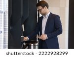 Small photo of Young businessman in suit pours favourite beverage, uses vending machine in office cafeteria or self-service automated retail place for comfort and busy life, start working day with cup of hot coffee