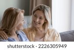 Small photo of Woman hugs 50s mom talking seated on sofa. Mature female enjoy communication to young adult daughter, family lead trustworthy conversation relaxing, spend leisure at home. Bond, understanding, support