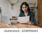 Small photo of Serious freelance business woman working on report at home, reading document at home office table with laptop, checking bill, invoice, agreement text, sales result, receiving official letter