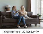 Small photo of Happy middle aged mom and pretty adult daughter chatting over cup of coffee, enjoying meeting, family leisure, sitting on home couch together, talking, holding mugs of hot drinks. Full length shot