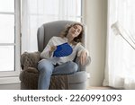 Small photo of Tired relaxed beautiful young woman suffering from heat, hypoxia, stuffy air, cooling hot air, waving paper handheld fan with closed eyes, feeling relief, resting in armchair at home