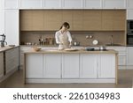 Happy young baker girl preparing pizza, pie, dropping grated cheese on rolled dough, baking in home kitchen modern interior, enjoying culinary hobby, cooking activity, smiling
