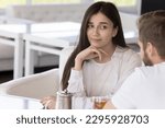 Small photo of Pretty millennial woman sit at table in cafe on dating with boring man, looks with him with disbelief and disinterest. Bad first impression, problems in relationships, unsuccessful speed blind dating