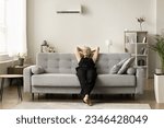Small photo of Positive homeowner woman enjoying leisure, ventilation, comfortable cool air temperature under conditioning split system at home, resting with closed eyes on soft stylish couch