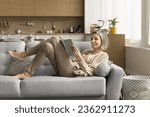 Small photo of Cheerful mature reader enjoying bestseller, leisure, relaxation, home education, reading paper book in white empty cover, resting on couch, laughing, having fun, studying, doing homework