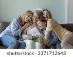 Small photo of Cheerful girls and women congratulating eldest great grandma on birthday, giving flowers, hand drawn greeting card with heart from kid. Four female family generation hugging, celebrating mothers day