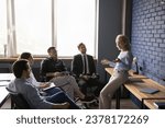 Middle aged woman leader stand in office explain work task, discuss project, present new creative idea or plan. Positive older coach gives seminar to young employees, Teambuilding, mentoring, business