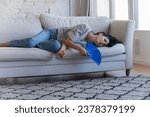 Small photo of Sick frustrated adult homeowner woman getting heat stroke, lying on sofa, waving handheld paper fan, suffering from hot stuffy air, exhaustion, hypoxia, feeling overheated, bad, ill