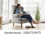Middle-aged woman relax on comfortable armchair in living room with laptop, watch movie on digital streaming on-line services, spend time on internet, make order, enjoy leisure and modern tech usage