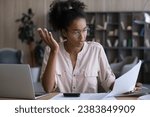 Small photo of Serious Black woman reading and checking wrong financial papers, bills for paying with mistakes. Confused puzzled accountant reviewing tax documents for payment at workplace with laptop