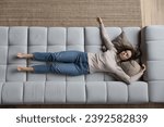 Young overworked woman looks drained, deprived of strength or vitality resting, sleeping alone at home lying on cozy sofa after hardworking, above view. Housewife and chores, exhaustion relief concept