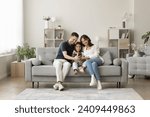 Small photo of Positive young mom, dad and sweet girl kid taking family selfie on cozy comfortable couch, having fun with digital gadget in cozy stylish home interior, using smartphone for selfie together