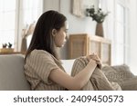 Sad lonely young woman looking away sitting on sofa at home, looks pensive, suffer from depression, personal problems, have melancholic mood, think about break up, negative emotions, stress, burnout