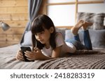 Internet addiction and safety. Curious preteen girl stay at home alone lie on bed surf websites on smartphone online read blogs watch web video channels. School age child relax browsing social media