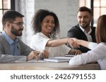 Small photo of Business ethics and etiquette. Gender and ethnic diversity at work. Smiling young African-American woman shaking hands with negotiation partner, sitting at desk with male teammates in company meeting