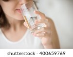 Happy beautiful young woman drinking water. Smiling caucasian female model holding transparent glass in her hand. Closeup. Focus on the arm
