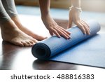Close-up of attractive young woman folding blue yoga or fitness mat after working out at home in living room. Healthy life, keep fit concepts. Horizontal shot