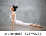Beautiful young woman wearing white sportswear set and smartwatch working out against grey wall, doing yoga or pilates exercise. Upward facing dog pose, Urdhva mukha shvanasana. Full length