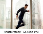 Busy businessman hurrying up to come at meeting on time in office building, blurred silhouette running in hurry along hallway, looking on wristwatch on the move, window city view at background 