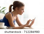 Small photo of Young attractive woman using digital tablet at home, enjoying useful mobile apps for study and entertainment, choosing goods in online store, reading interesting e book, checking news feed, side view