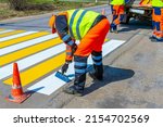 A road worker paints, repairs a pedestrian crossing on an asphalt surface on a city street.