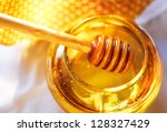 Small photo of Honey dipper on the bee honeycomb background. Honey tidbit in glass jar and honeycombs wax.