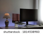 Computer workstation ideal for the home office consisting of a gray laptop on a stand, a large curved and black monitor, a white lamp, a white keyboard and a white optical mouse with backlighting