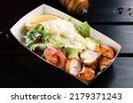 Caesar salad in lunchbox on wooden background, Food delivery: classic caesar salad with grilled chicken fillet in a takeaway box