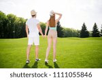 He vs She together forever! Rear view fullbody portrait of attractive lovely couple in shorts sneakers straw hats holding hands walking outside enjoying beauty of landscape trees