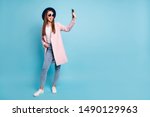 Small photo of Full size photo of childish girl using her cell phone taking self photo having fun wearing eyeglasses eyewear topcoat denim jeans isolated over blue background