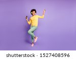 Full length body size photo of trendy stylish cute free girlfriend wearing green pants trousers yellow sweater footwear in headphones listening to music dancing isolated violet pastel color background