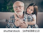 Closeup photo of funny two people old grandpa little granddaughter sitting sofa stay home quarantine safety hugging piggyback modern design interior living room indoors