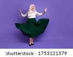 Full body photo of attractive mature grey haired lady dancing retro party raise hands modern movement excited wear white blouse green long skirt flying isolated purple color background