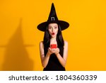 Halloween almost canceled. Photo of cute lovely young magician lady hold telephone amazed theme event postponed wear black wizard headwear dress isolated bright yellow color background