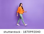 Full length body size photo of young girl walking forward in green pants sweater looking copyspace isolated on vivid purple color background