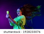Small photo of Photo of amazed shocked young woman look phone fast internet fly hair isolated on colorful neon background
