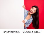 Portrait of attractive cheerful curious girl holding big blank poster ad promo isolated over bright red color background