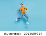 Photo of funky cute young man wear yellow sweater smiling jumping high showing thumbs up isolated blue color background