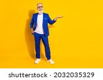 Full size photo of positive grey beard old man hold empty space wear spectacles blue jacket isolated on yellow background