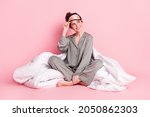Portrait of attractive dreamy cheerful girl in pajama sitting on bed linen isolated over pink pastel color background