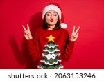 Photo of shiny flirty young woman wear ornament sweater sending you kiss showing v-signs enjoying christmas isolated red color background
