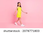 Full length photo of cute charming school girl wear yellow dress dark eyewear walking empty space isolated pink color background