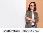 Small photo of Photo of cheerful lady direct forefinger placard board empty space wear specs khaki shirt isolated beige color background